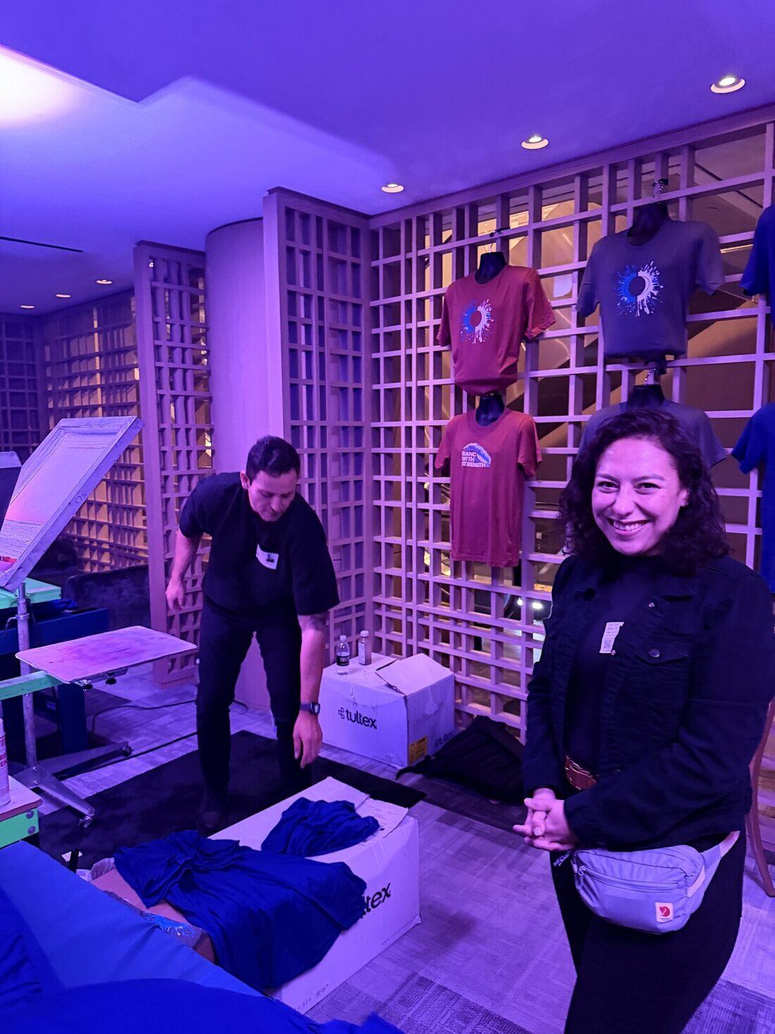 Two crew members staging boxes of garments in front of a display wall